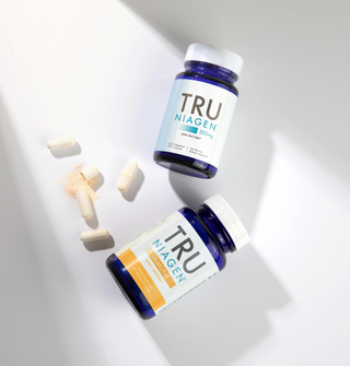 Two blue bottles with white labels, one labeled TRU NIAGEN IMMUNE and the other TRU NIAGEN 300mg, and capsules, against a white background.