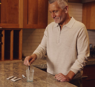A man in a kitchen stirring a drink made with a Tru Niagen stick pack.