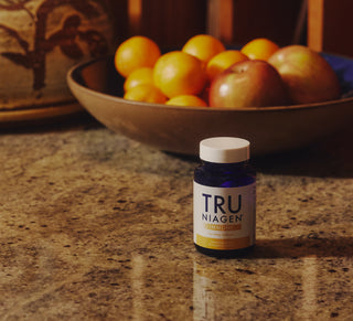 TRU NIAGEN supplement bottle on a countertop with fruits in the background.